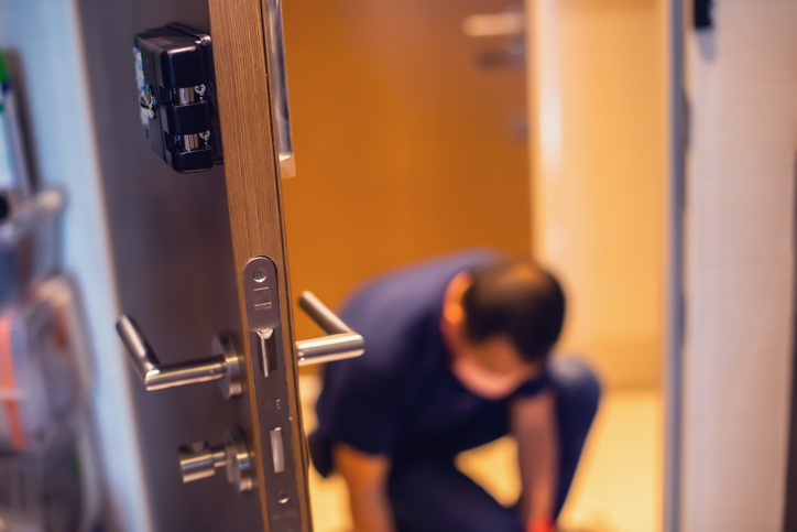 Selective focus to black digital door lock security plate with blurry technician.